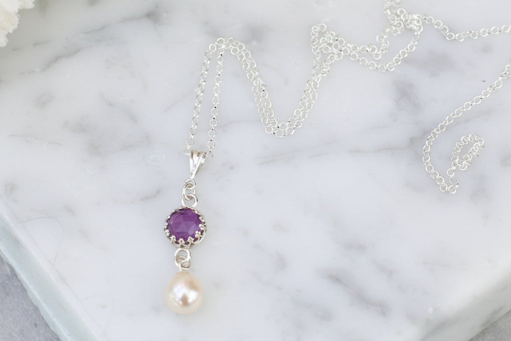 Necklace with a purple gemstone and pearl pendant on a marble surface.