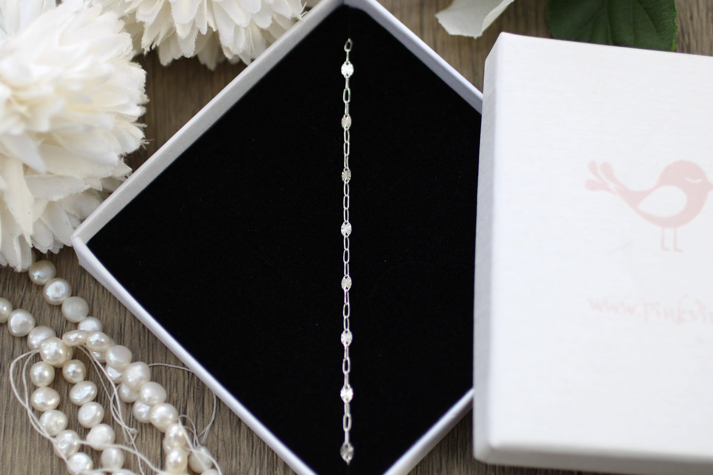 Silver bracelet in a jewelry box with white flowers and pearls on a wooden surface