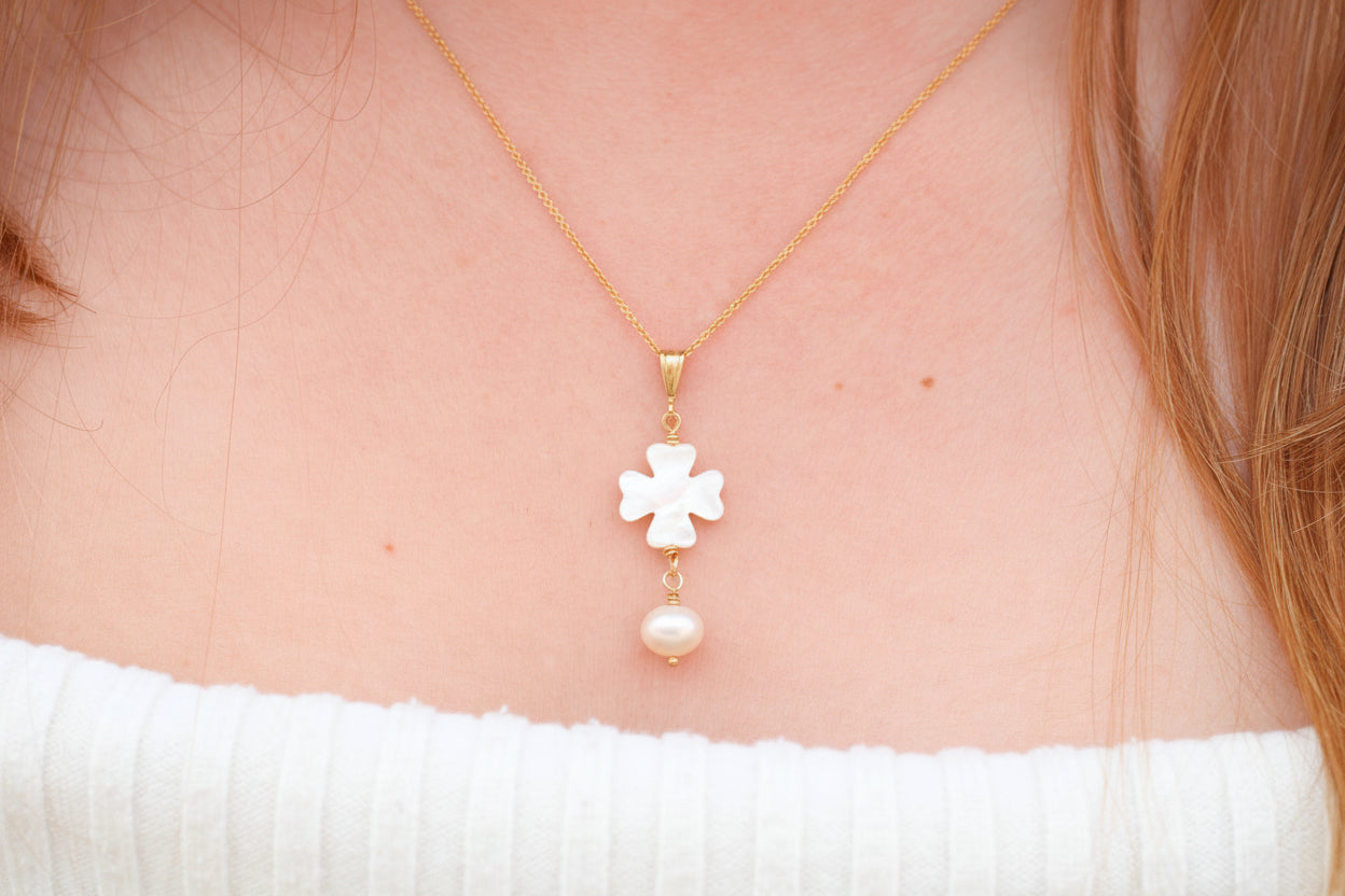 Gold necklace with a cross pendant and pearl on a person wearing a white top.