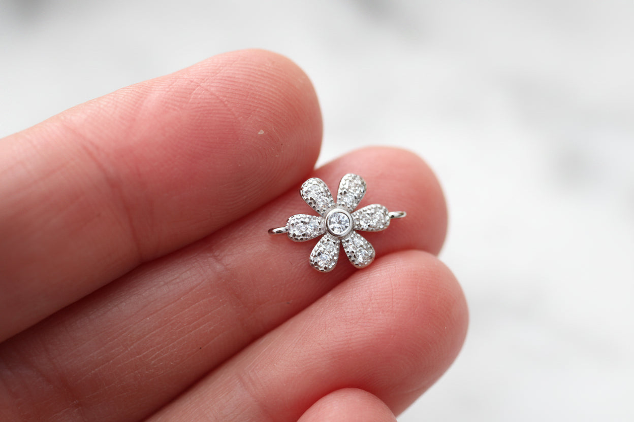 Silver flower-shaped earring held between fingers against a light background