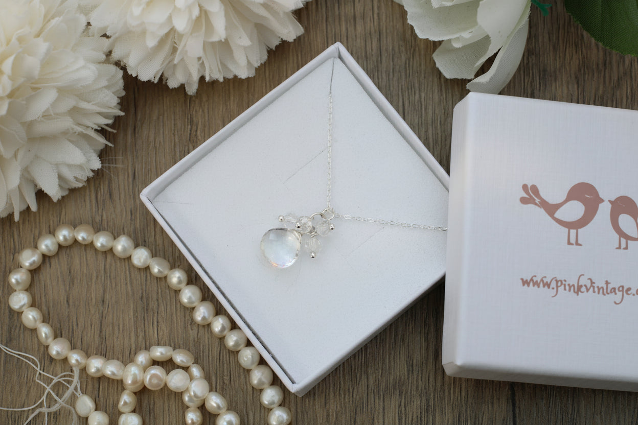 Necklace with a heart-shaped pendant in an open jewelry box on a wooden surface with flowers and pearls.