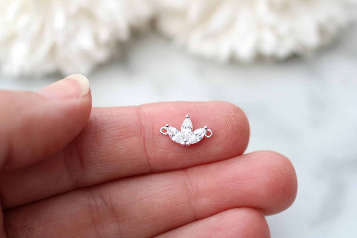 A small silver butterfly-shaped jewelry charm with clear rhinestones, held on the tip of a person's finger to show its tiny scale.