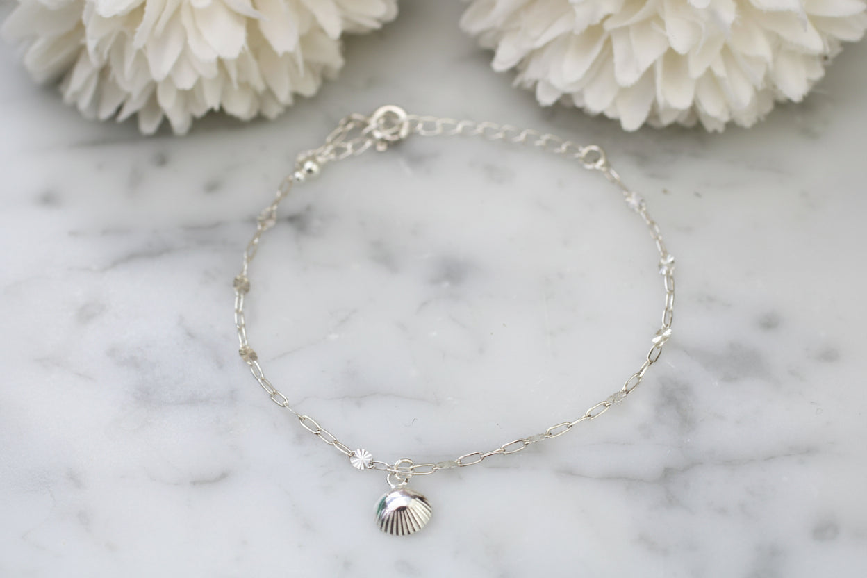 Silver bracelet with a shell charm on a marble surface