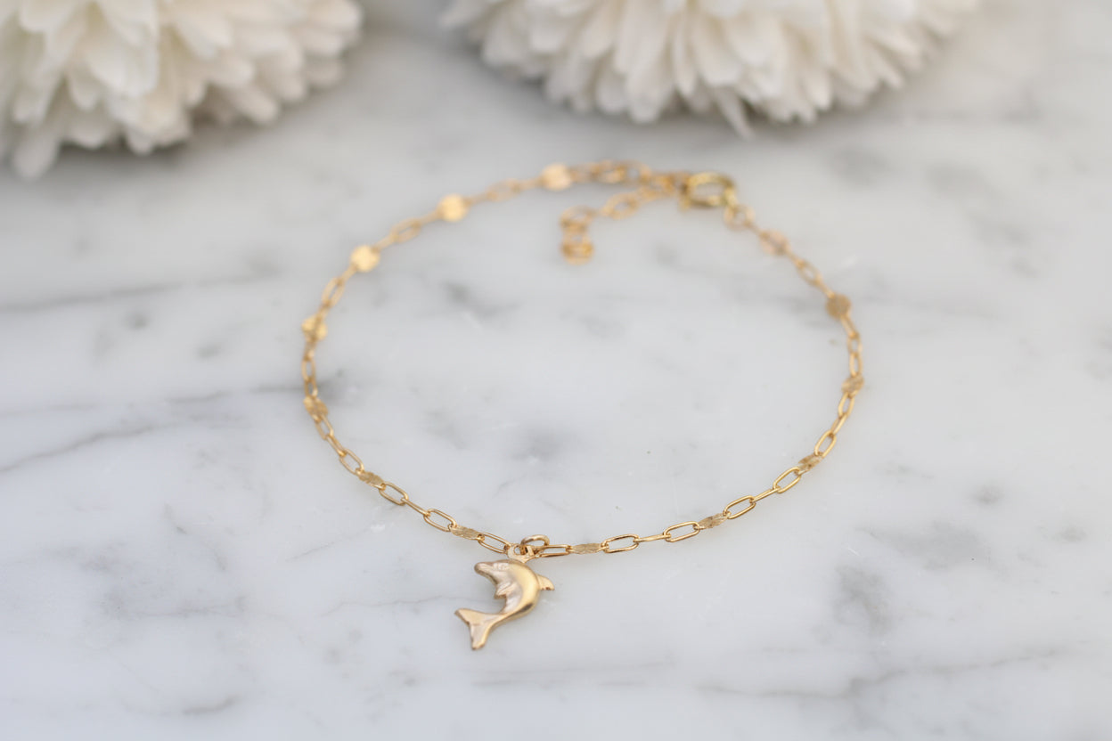 Gold anklet with a dolphin charm on a marble surface