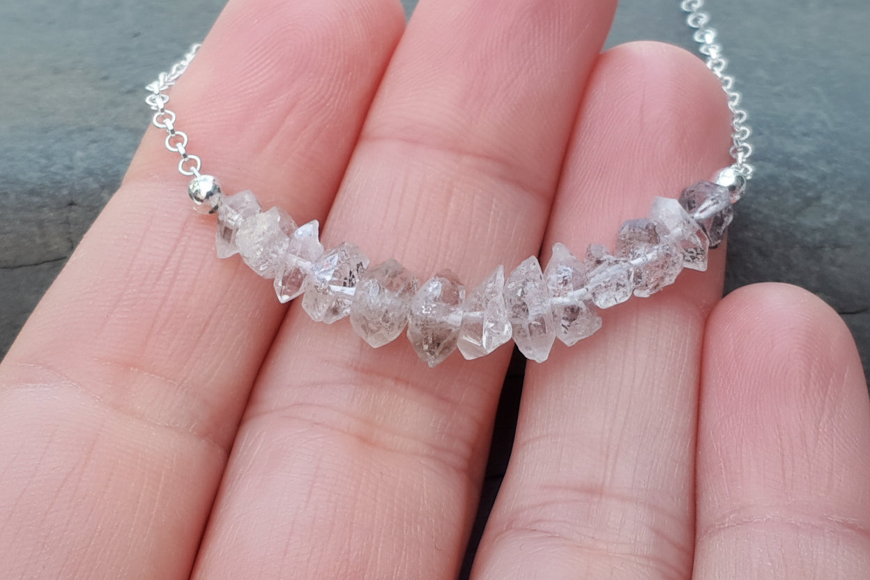 Crystal necklace held between fingers against a neutral background