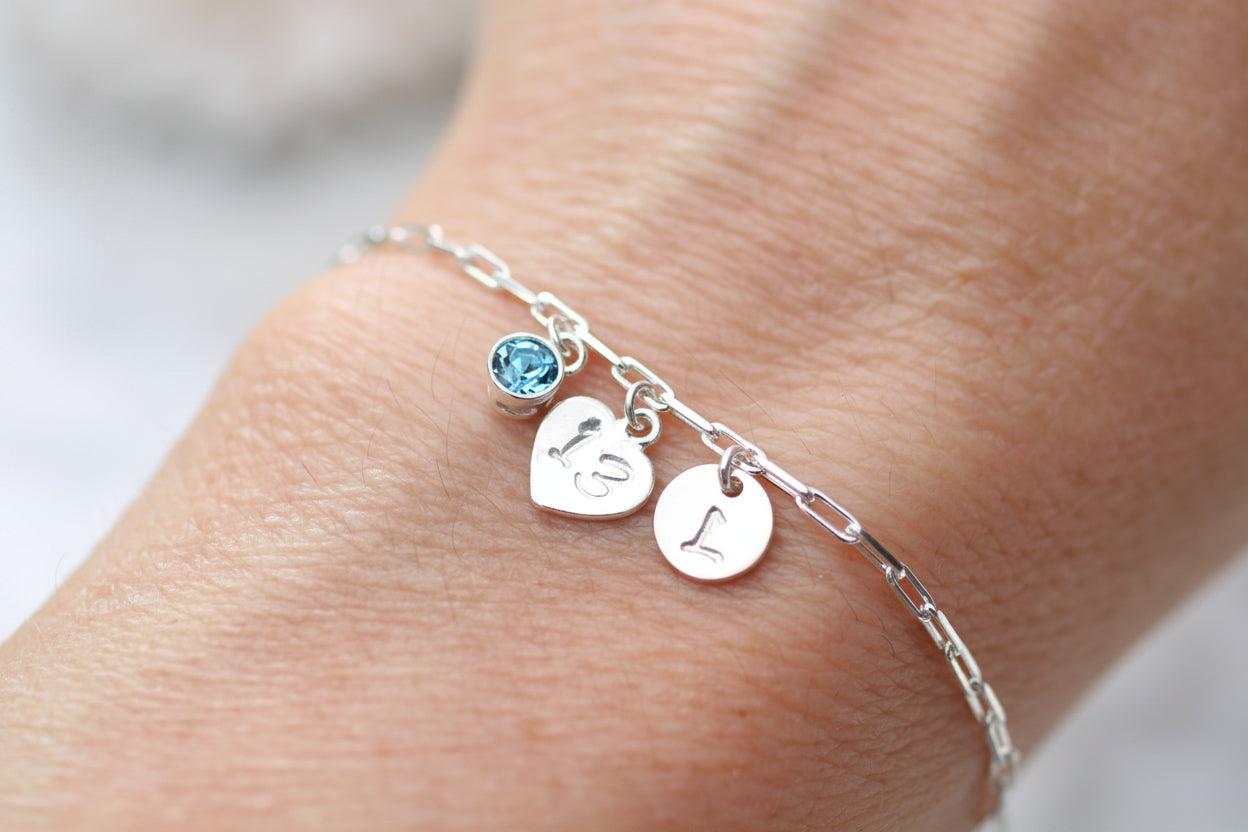 Silver bracelet with heart-shaped charms on a wrist against a neutral background
