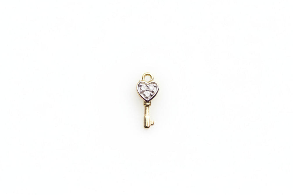 Gold key-shaped pendant with a heart on a light gray background