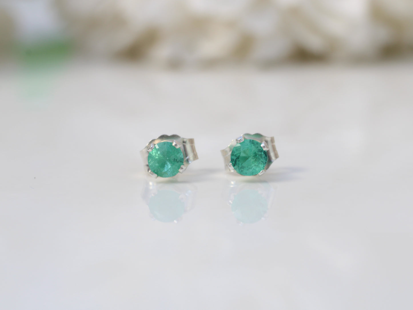 A pair of genuine emerald stud earrings set in silver or gold metal, displayed against a white background.