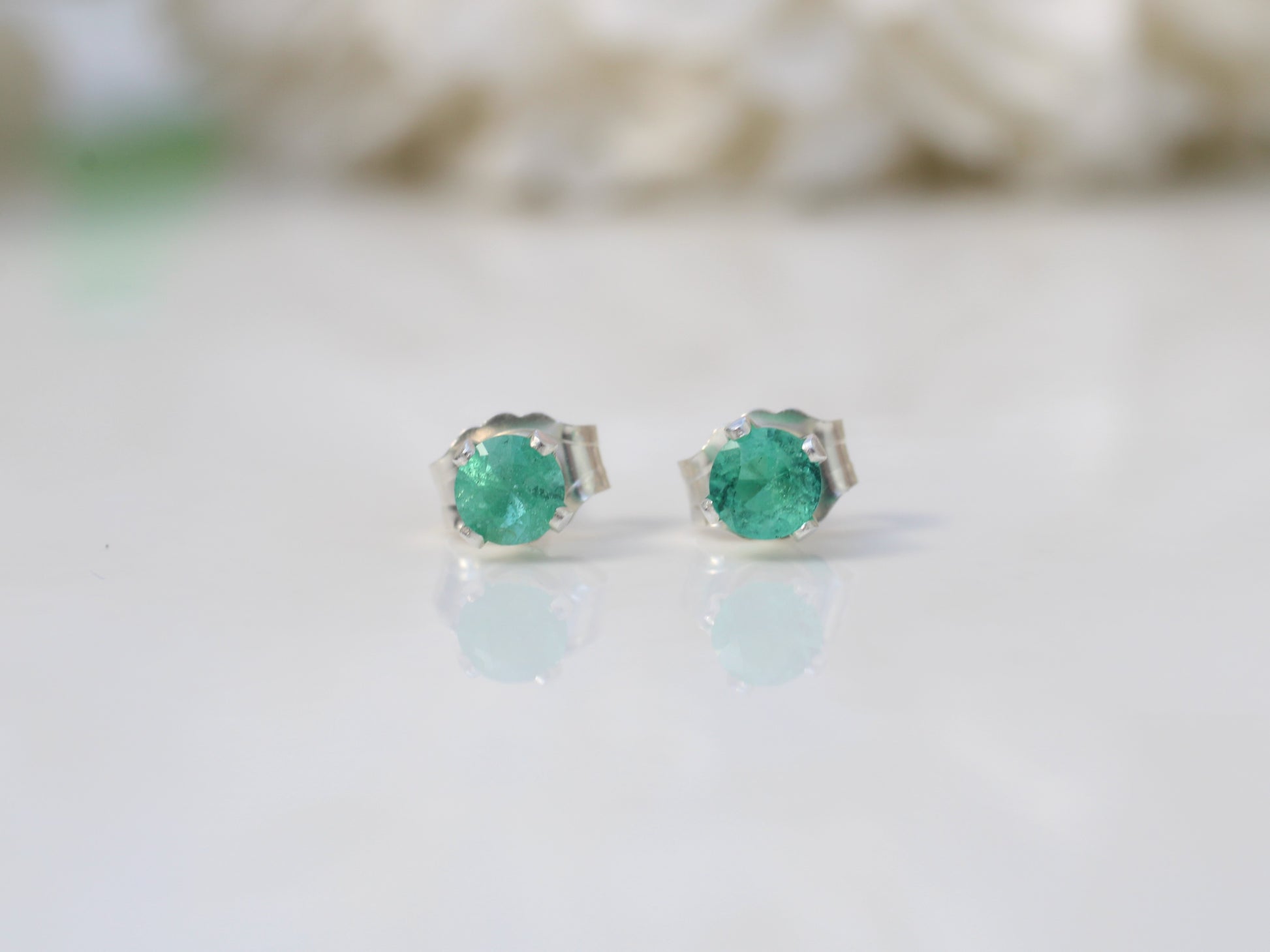 A pair of genuine emerald stud earrings set in silver or gold metal, displayed against a white background.