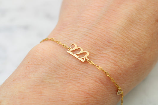 Gold bracelet with '222' on a wrist against a neutral background