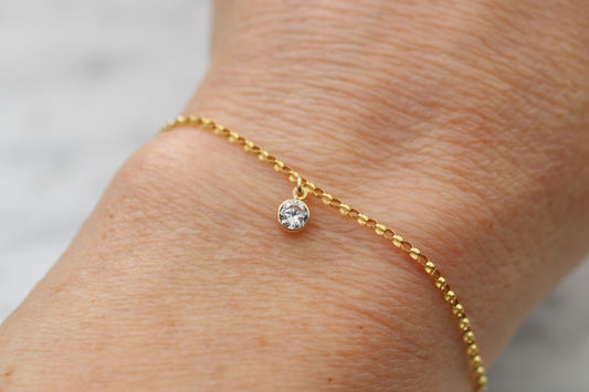 Gold bracelet with a clear crystal on a wrist against a neutral background