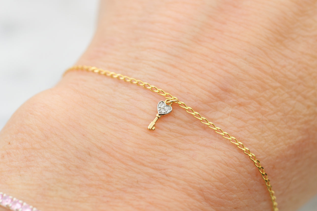 Gold bracelet with a heart-shaped key charm on a person's wrist.