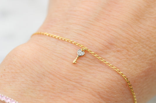 Gold bracelet with a heart-shaped key charm on a person's wrist.