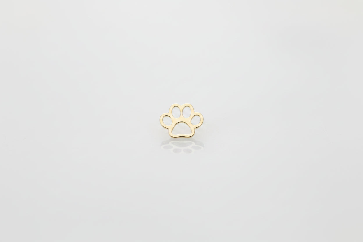 A small gold paw print charm or pendant lies centered on a light gray and white marble surface.
