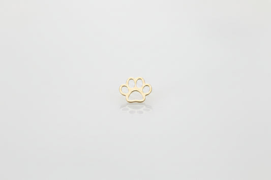 A small gold paw print charm or pendant lies centered on a light gray and white marble surface.