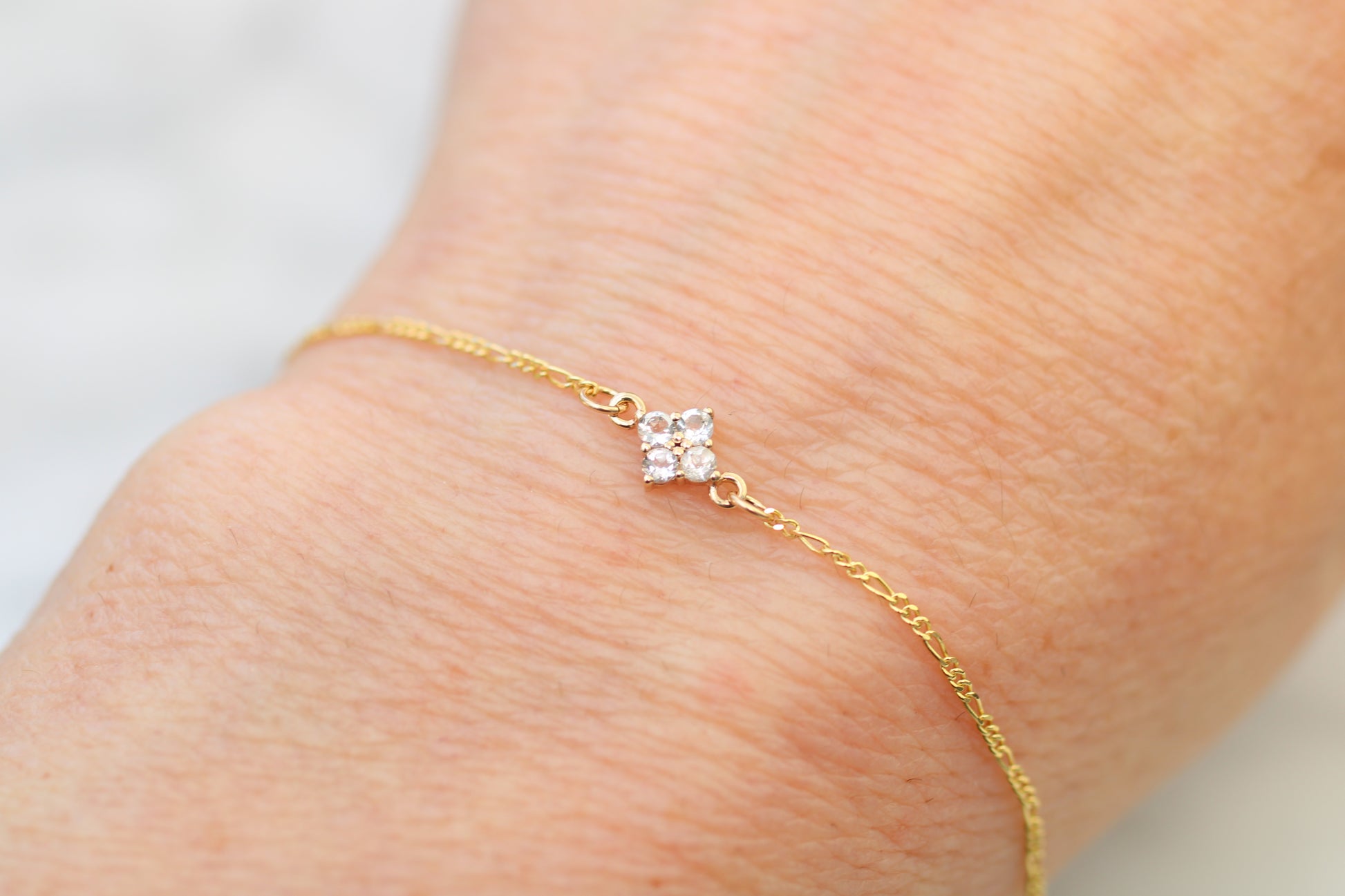 Gold bracelet with a clover on a wrist against a light background
