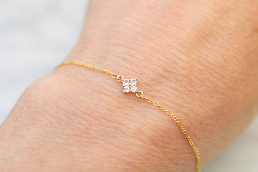 Gold bracelet with a clover on a wrist against a light background
