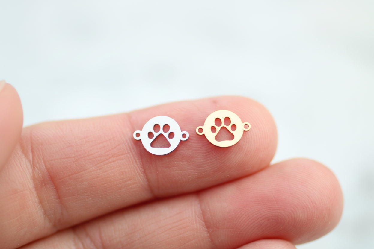 Two small silver paw print charms held between fingers on a light background