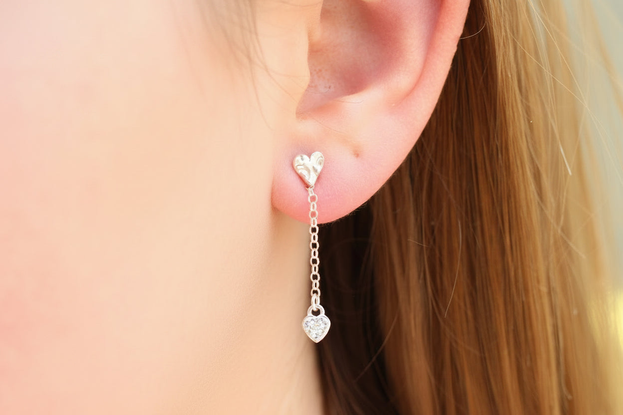 Close-up of an ear wearing a silver heart-shaped earring with a chain.