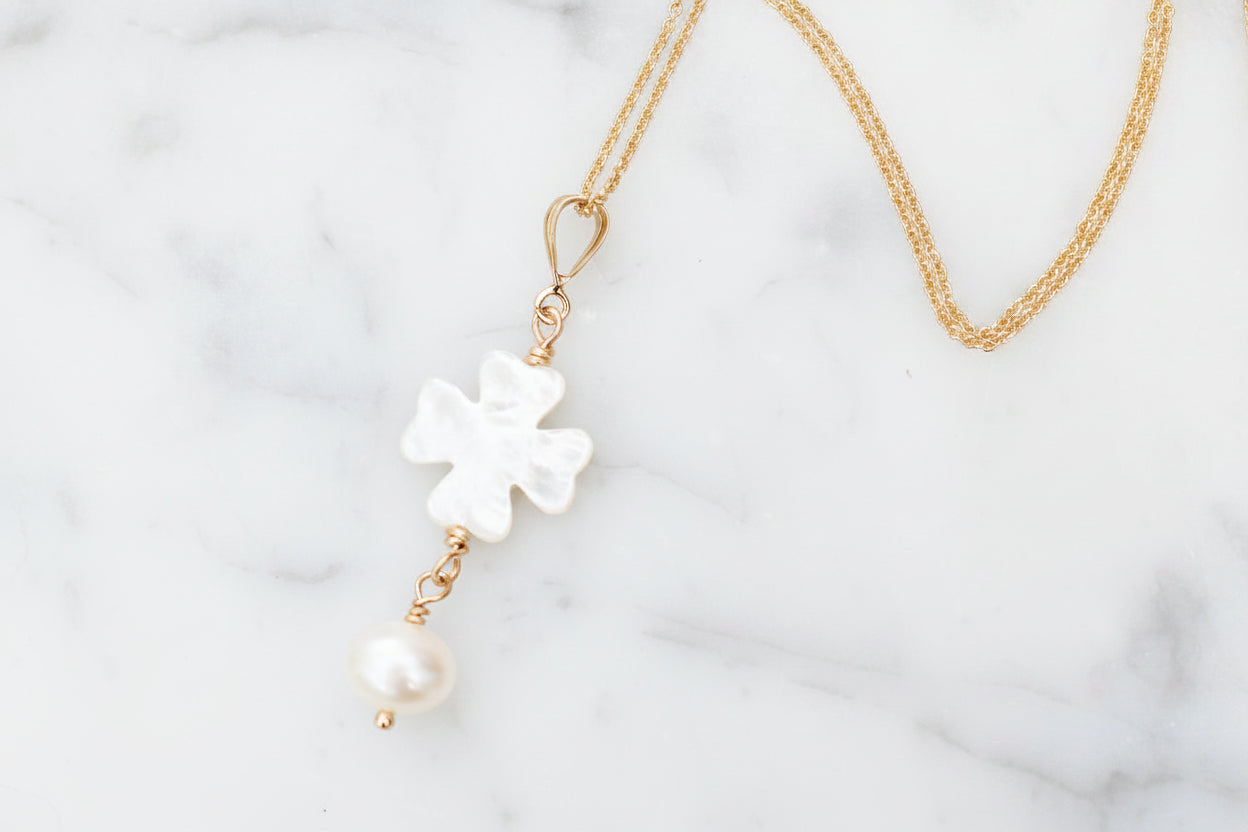 Delicate necklace with floral pendant and pearl drop on marble surface