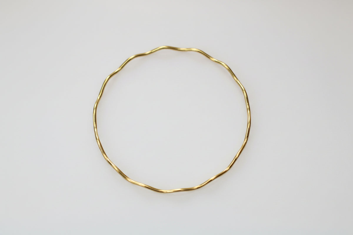 A thin, twisted gold wire bangle bracelet resting on a white and gray marble surface.