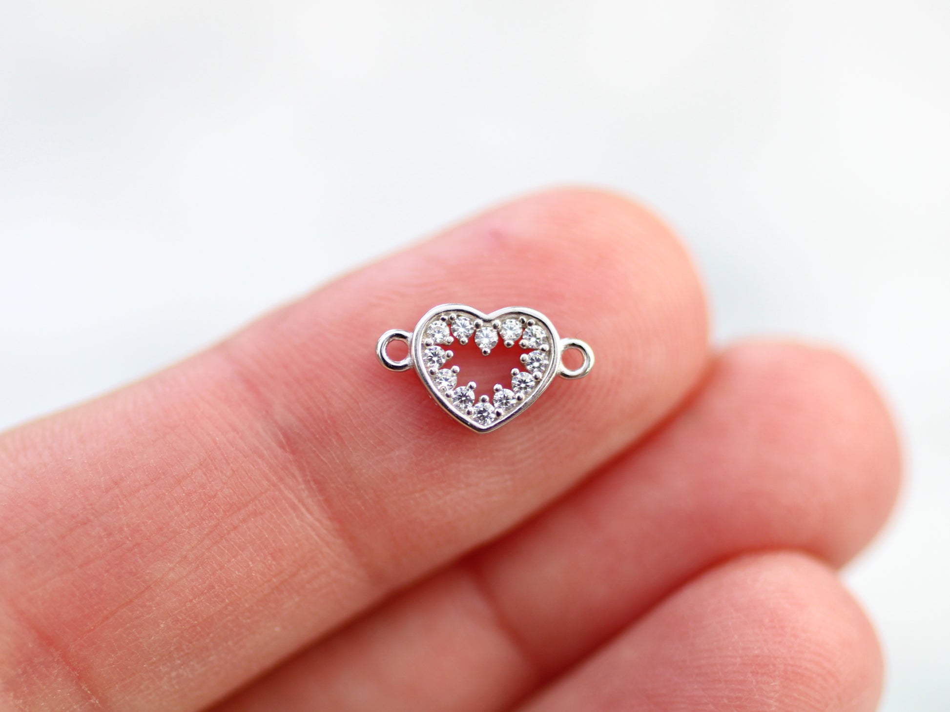 Silver heart-shaped jewelry clasp on a finger against a white background
