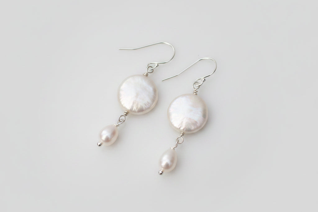 Pearl earrings on a marble surface with decorative elements.