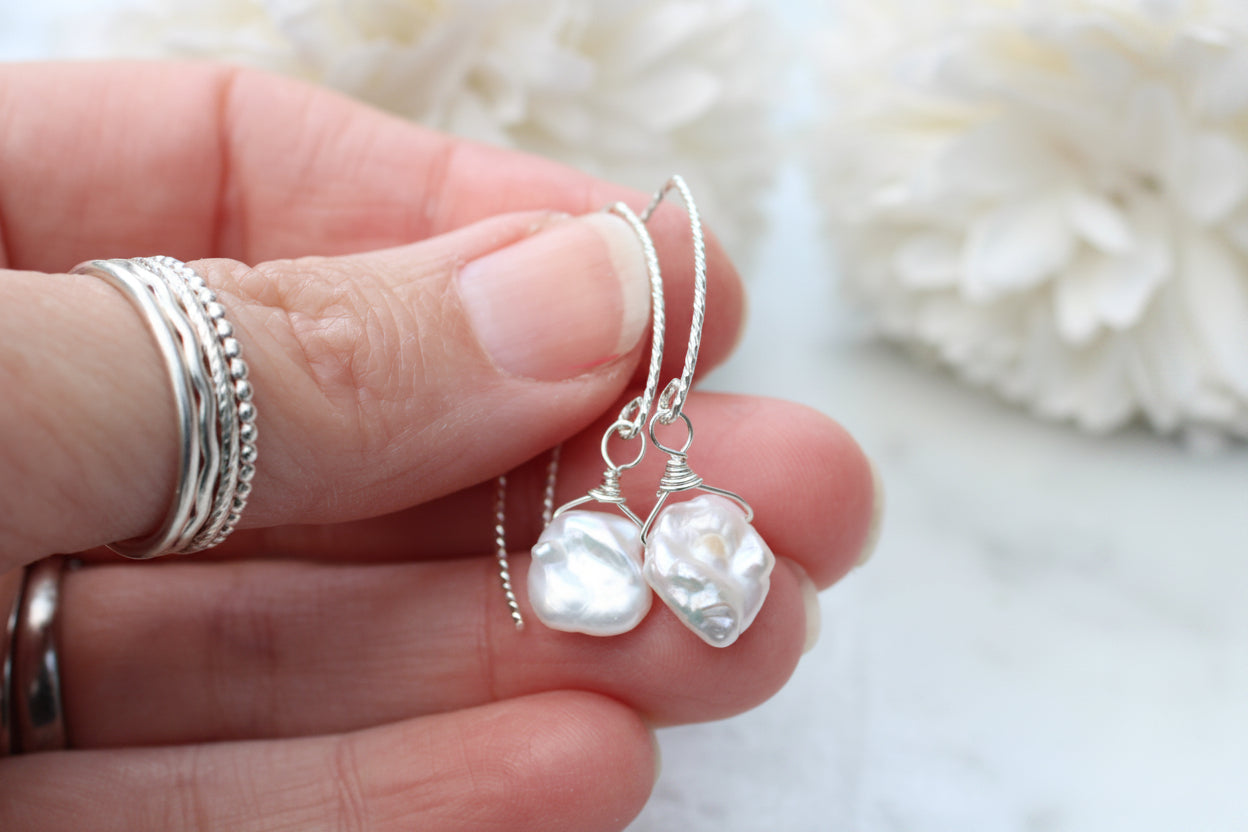 Pearl earrings held between fingers with a blurred white background
