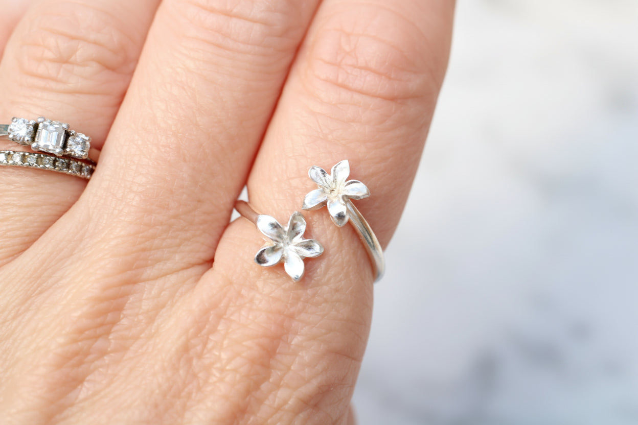 Silver flower-shaped rings on a person's finger with a blurred background