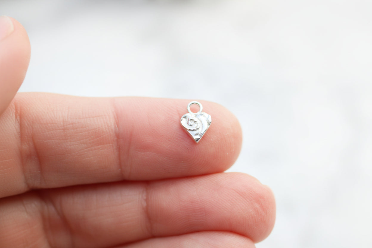 Silver heart-shaped charm held between fingers against a blurred background