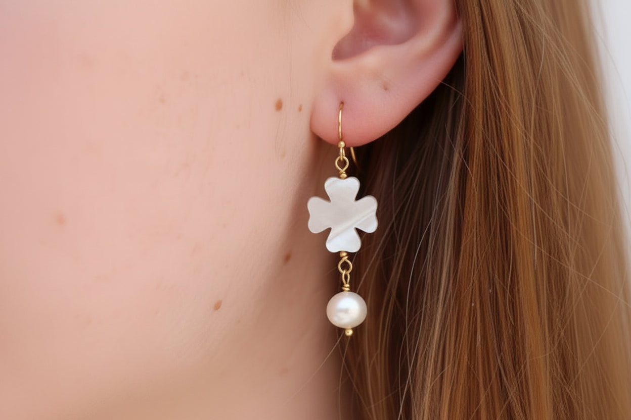 Close-up of a clover-shaped earring with a pearl drop worn by a person.