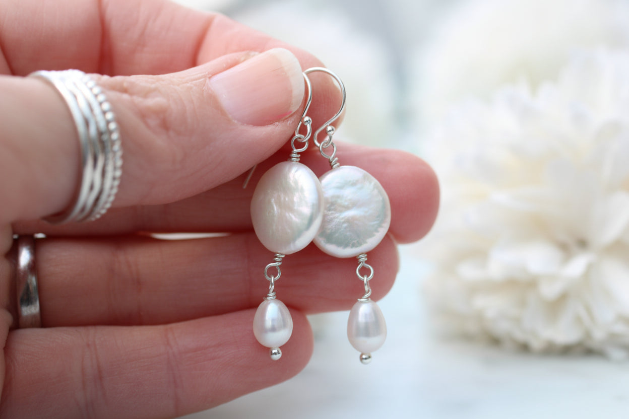 Pearl earrings held by a hand with silver rings on a blurred background