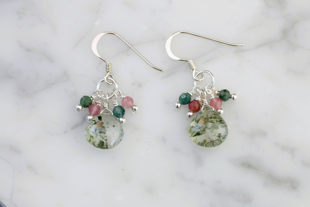 Pair of earrings with green and red gemstones on a marble background