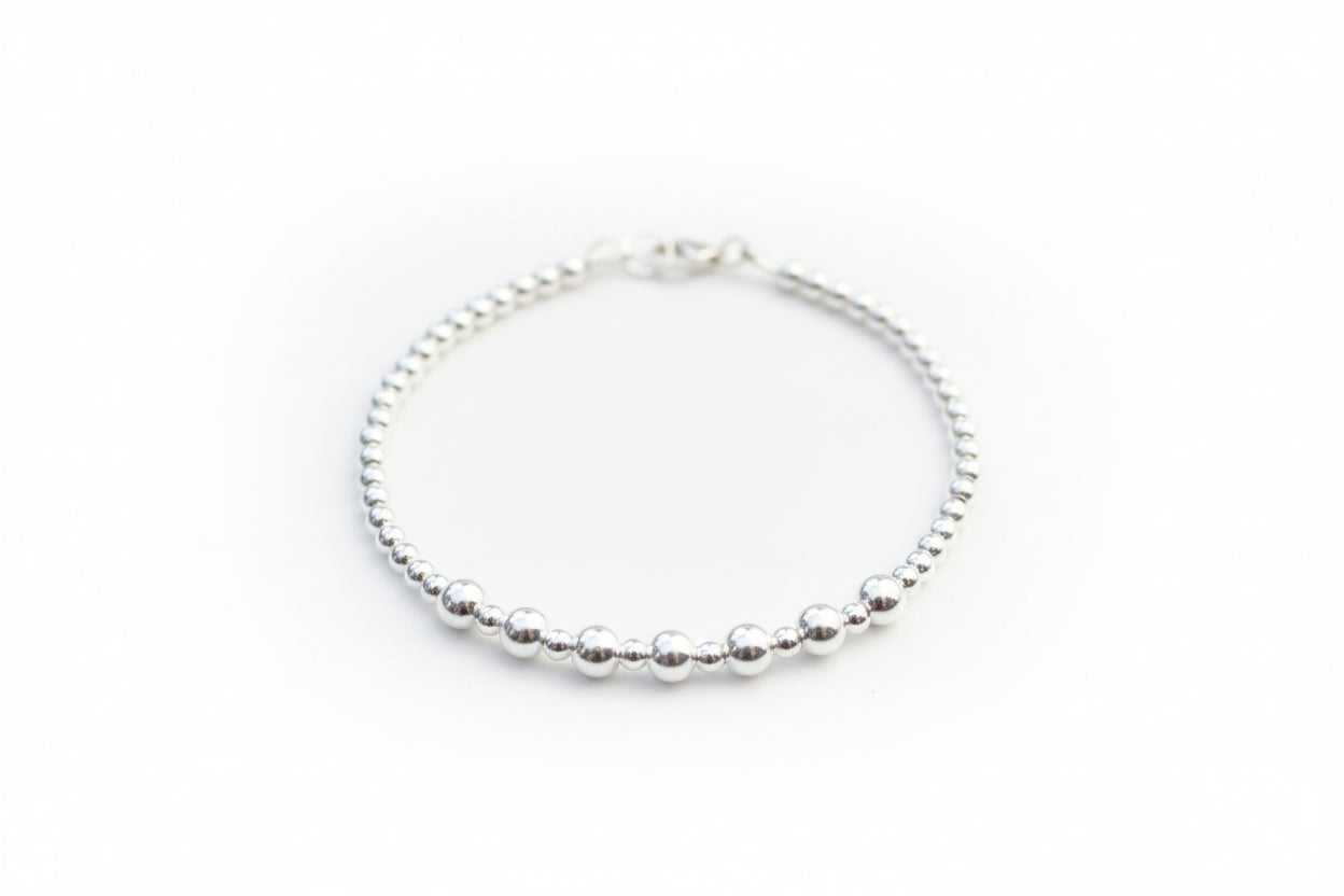 Silver beaded bracelet on a marble surface with a textured white stone in the background