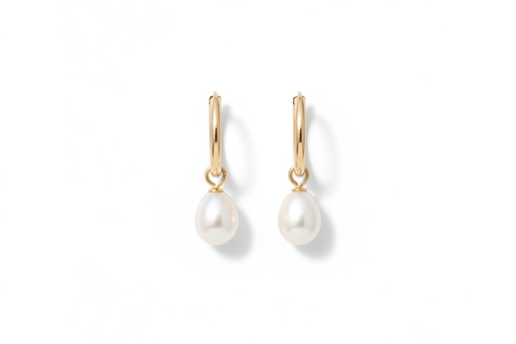 Gold hoop earrings with pearl drops on a marble surface with white flowers.
