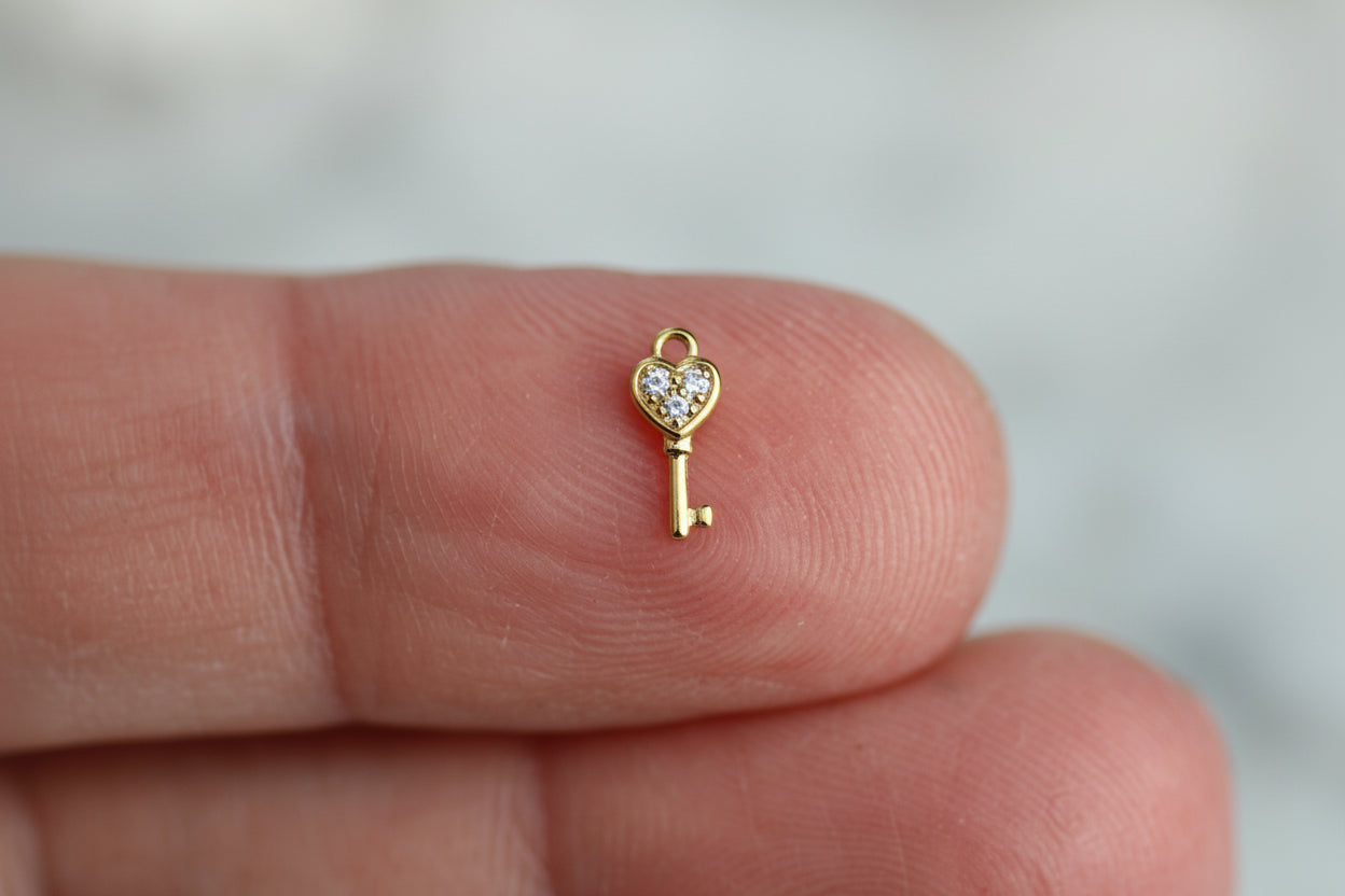 Small gold key-shaped charm with a heart on a finger against a blurred background