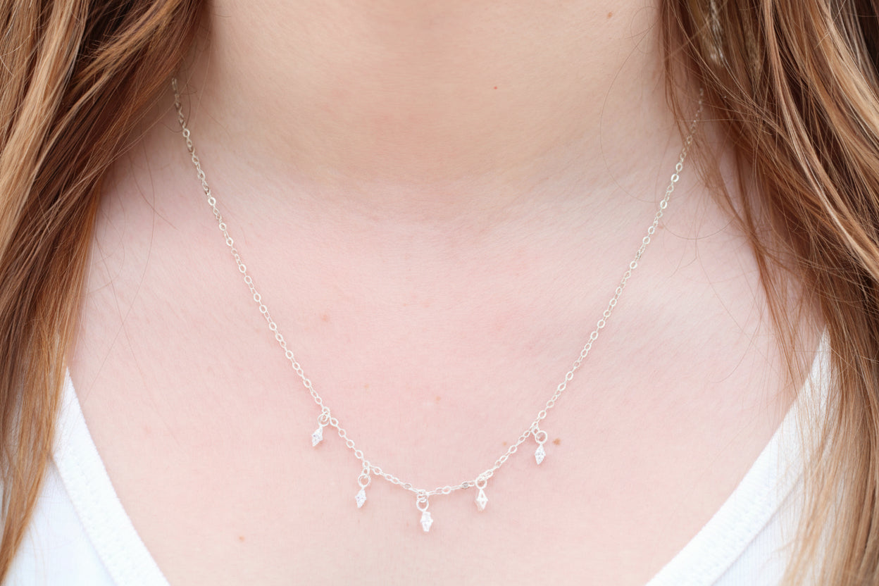 Necklace with small pendants on a person wearing a white top