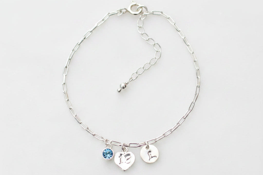 Silver bracelet with heart and blue gemstone charms on a marble background