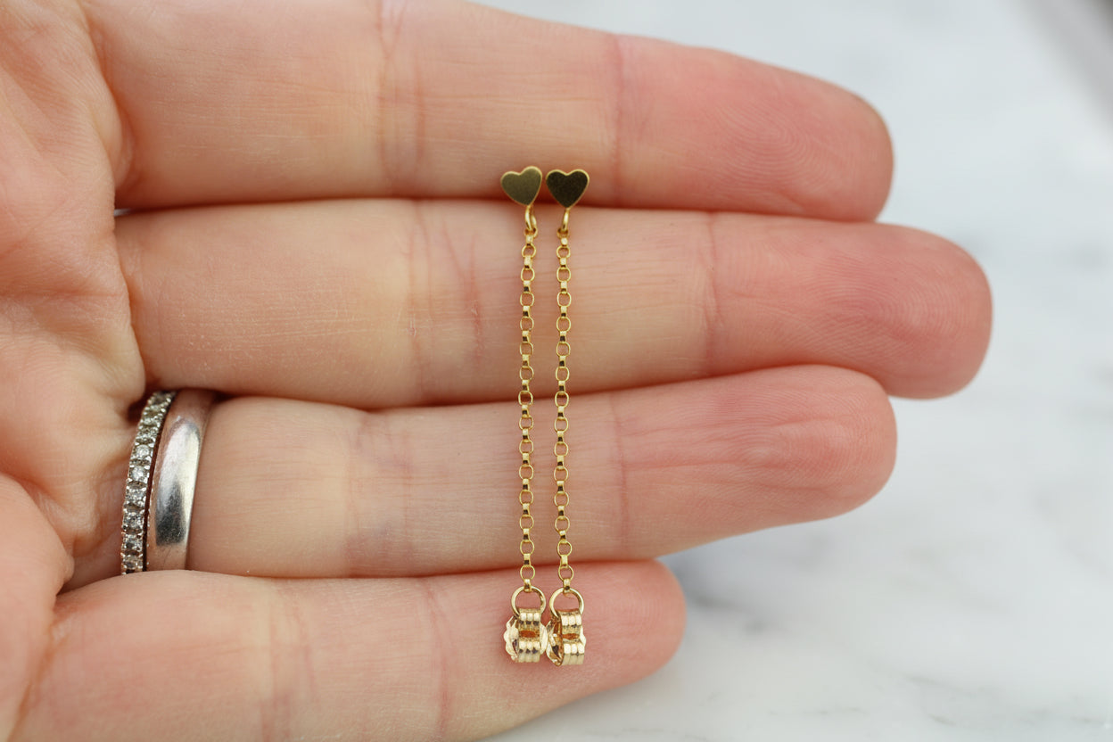 Gold heart-shaped earrings held between fingers with a blurred background