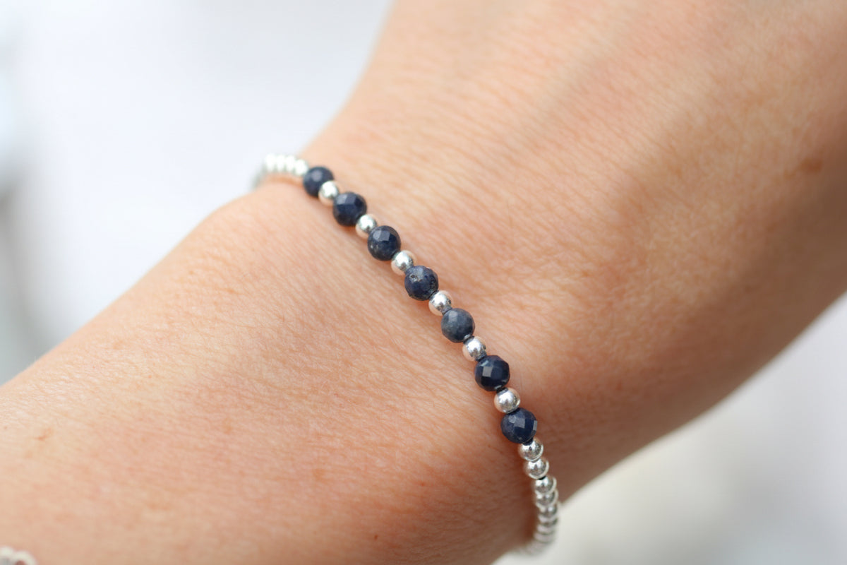 A delicate beaded bracelet with faceted navy blue beads and small silver spacer beads, shown worn on a person's wrist.