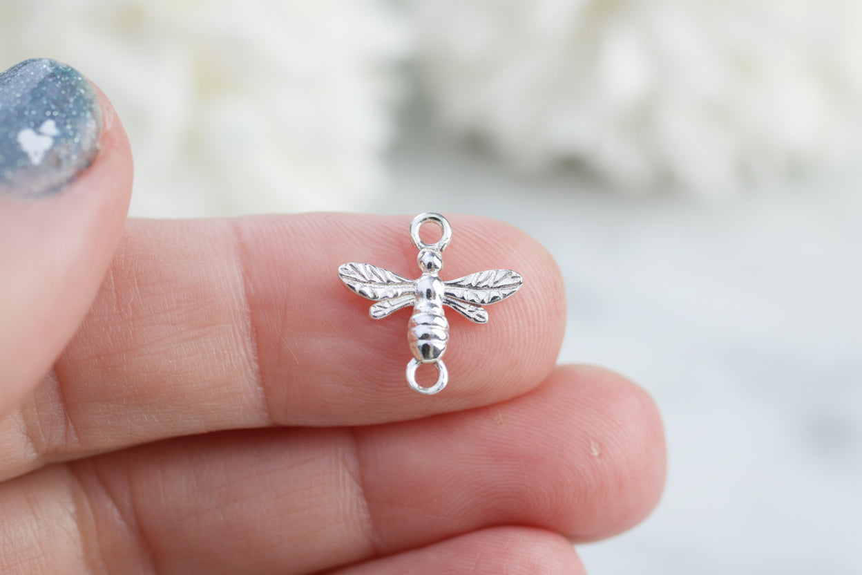 Silver bee charm held between fingers with a blurred background