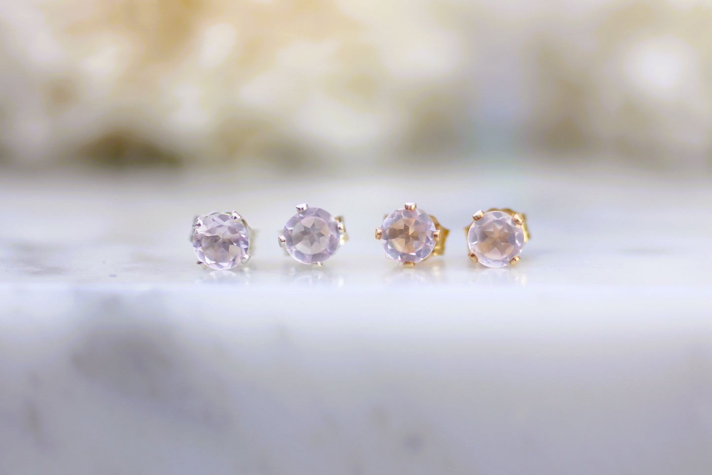 Four pink gemstone stud earrings on a marble surface with a blurred background