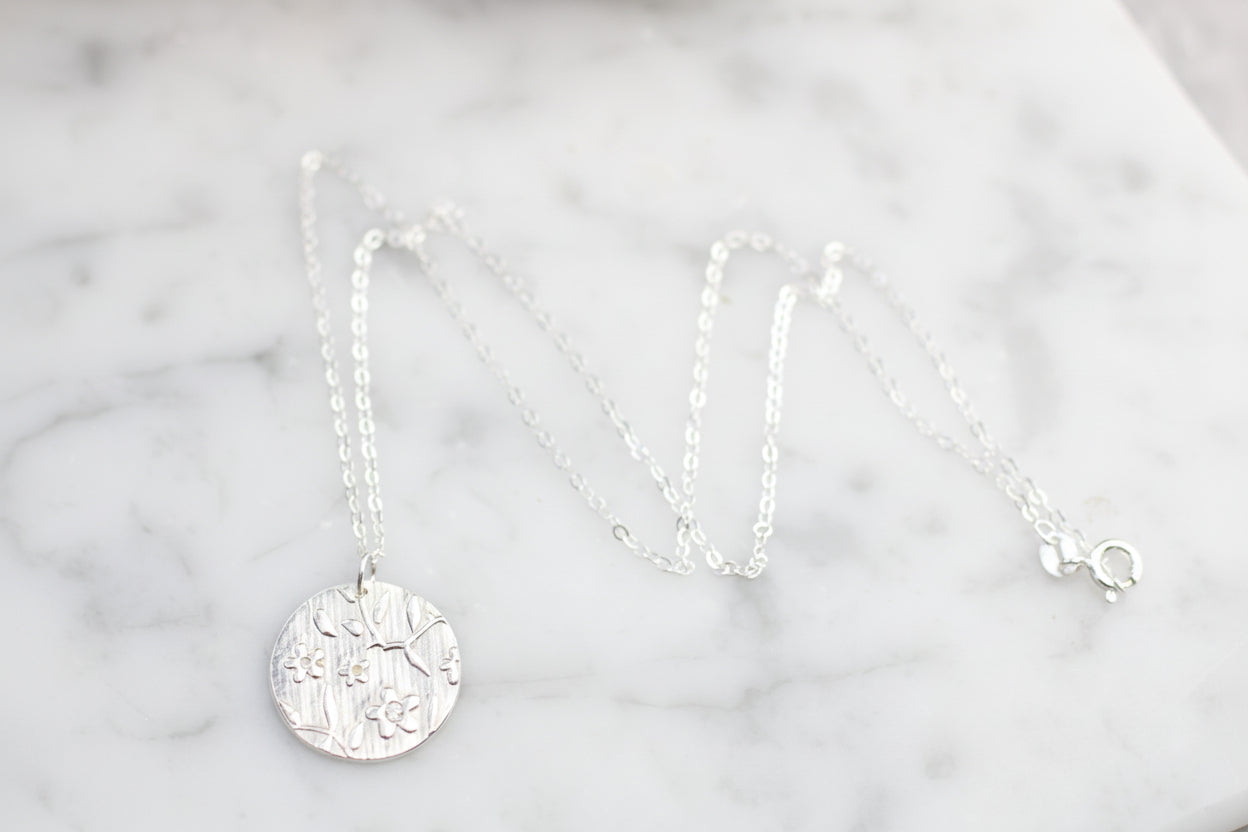 Silver necklace with a round pendant on a marble surface