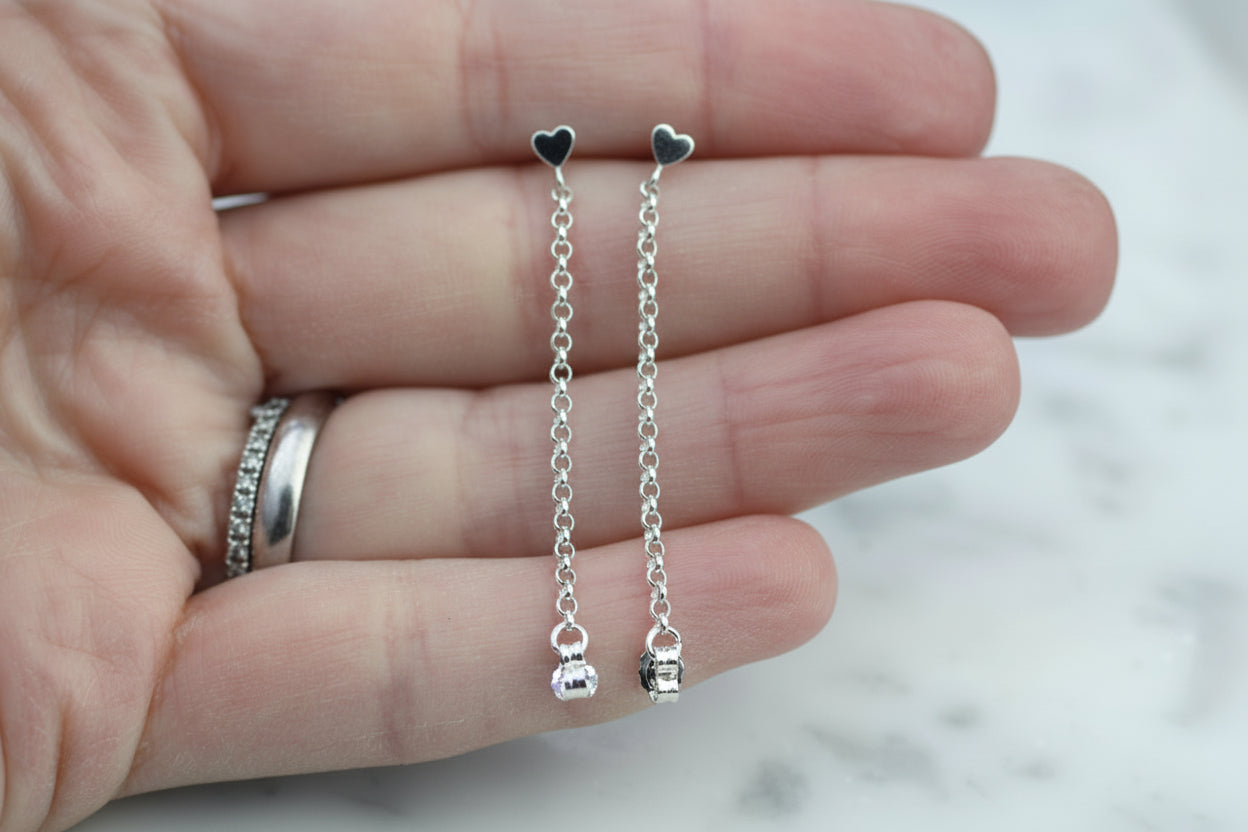 Silver heart-shaped earrings on a hand with a blurred background