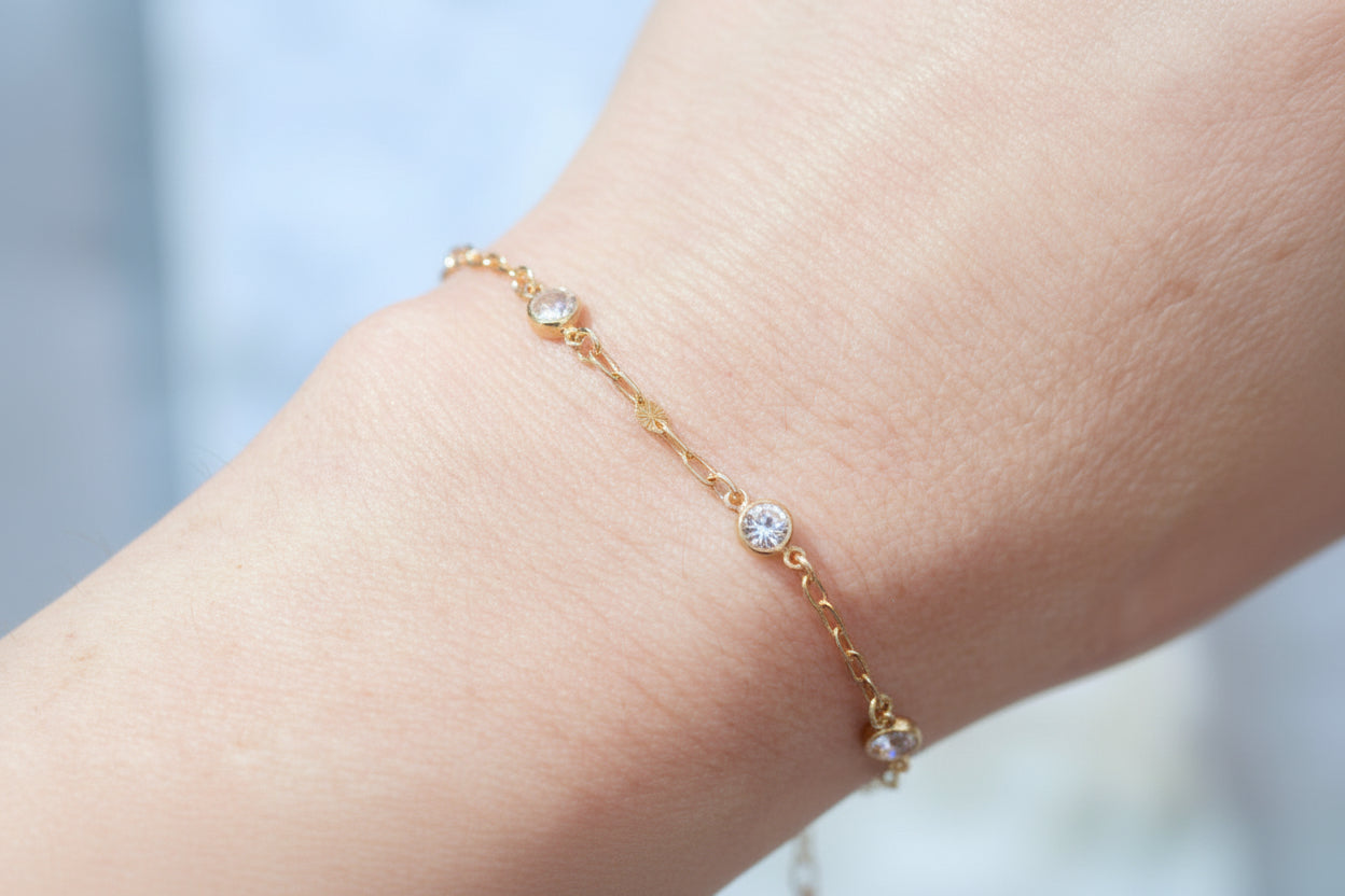 Gold bracelet with small stones on a wrist against a blurred background