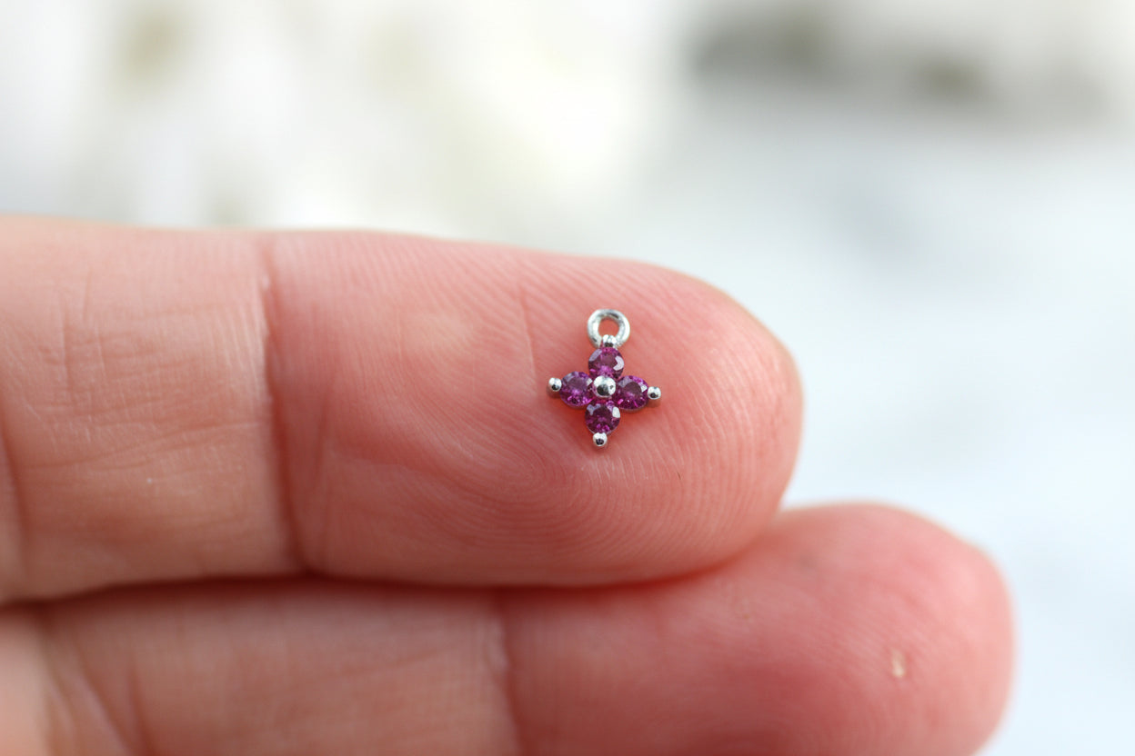 Small silver star-shaped charm with purple stones held between fingers against a blurred background