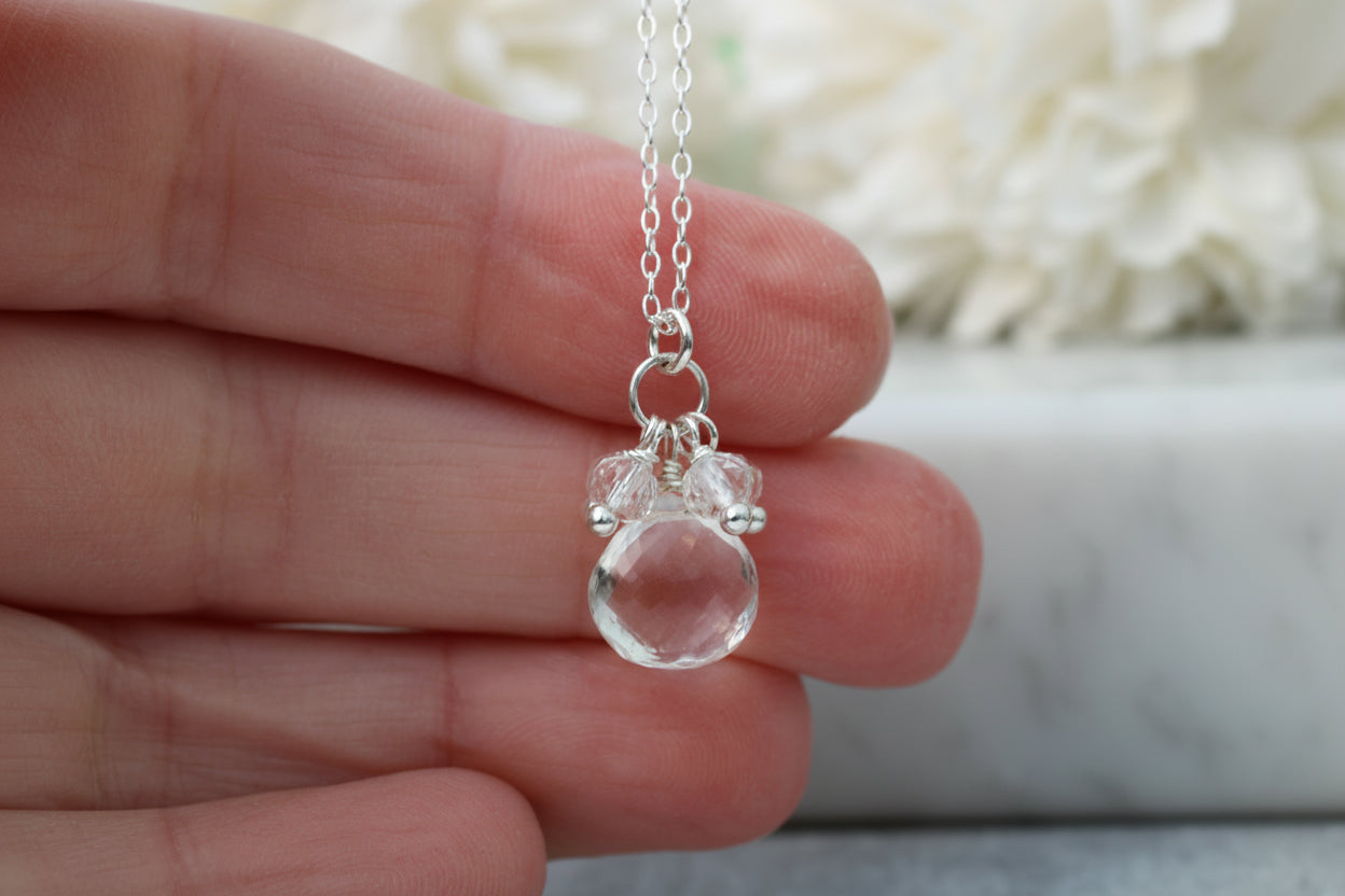 Clear teardrop pendant on a silver chain held in a hand with a blurred background