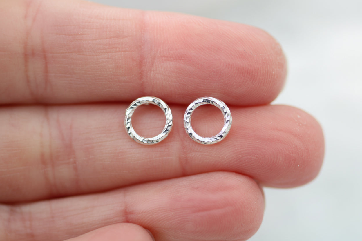 Silver hoop earrings held between fingers against a neutral background