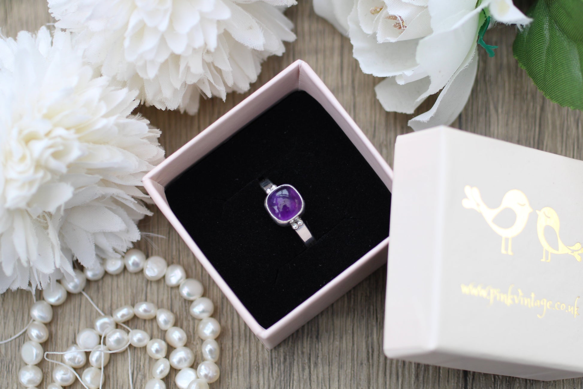 Amethyst ring in a box with white flowers and pearls on a wooden surface