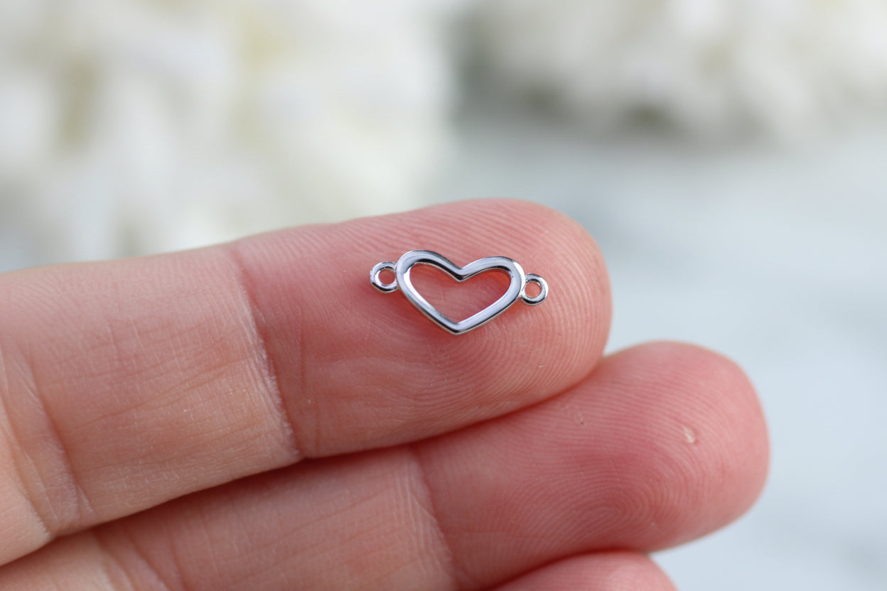 Silver heart-shaped jewelry piece held between fingers against a blurred background